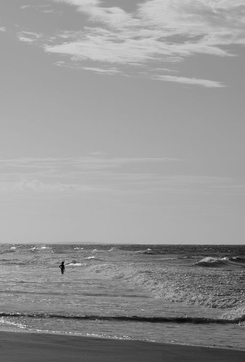 Free A lone figure stands by the shore, gazing at the summer sea under a vivid sky. Stock Photo
