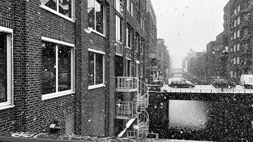 Snowfall over Buildings and River in City in Black and White