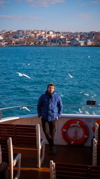 Man in blue jacket on a ferry cruising the Bosporus with Istanbul in the background.