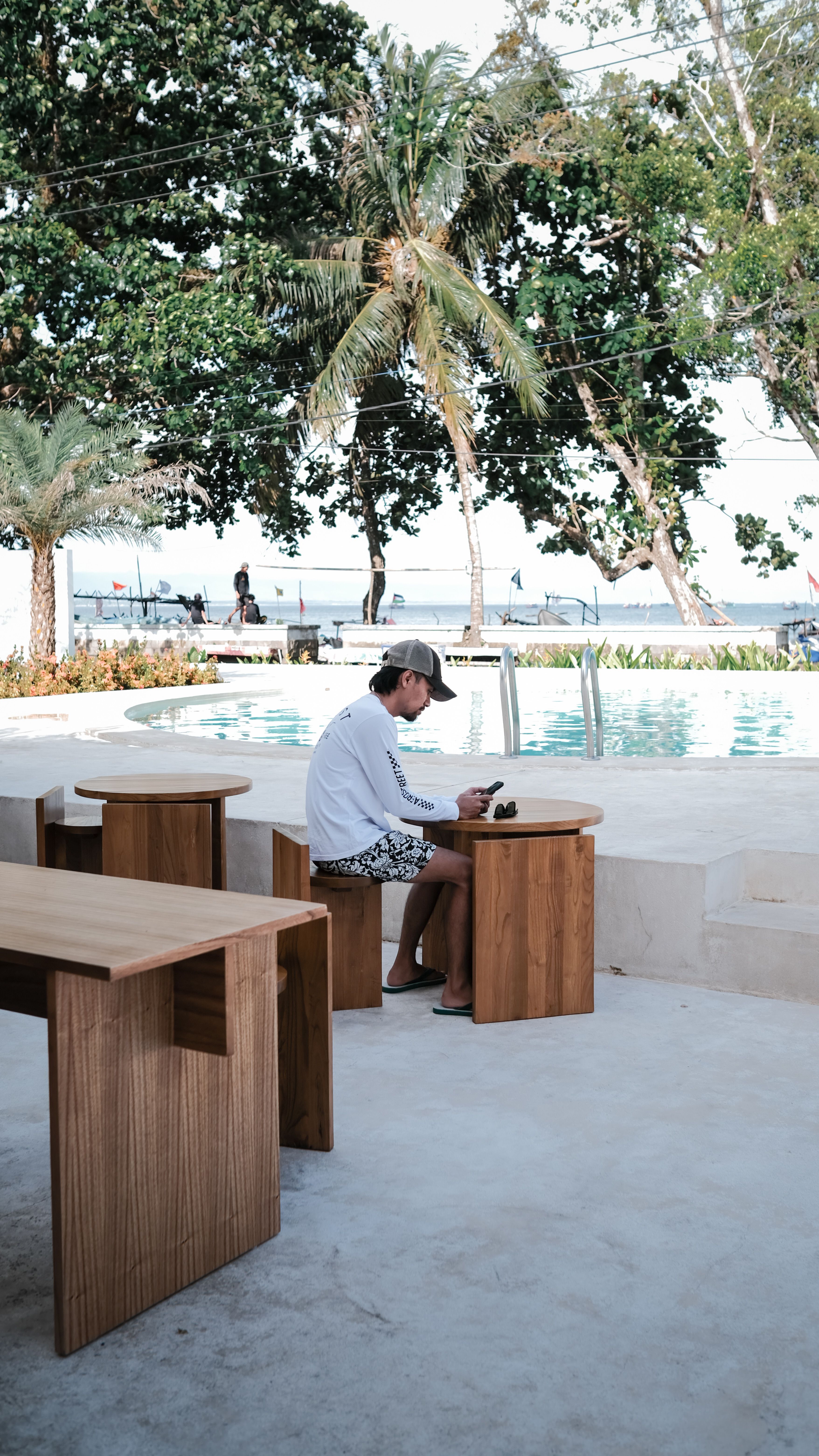 Man enjoying leisure time by the poolside in a tropical setting with wooden seating.