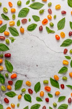 A vibrant display of cherry tomatoes and basil leaves on a cracked white surface, perfect for culinary backgrounds.