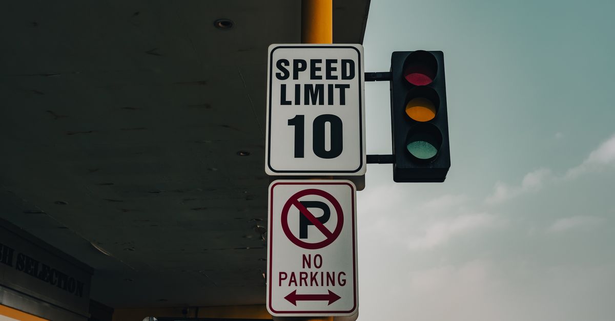 Close-up of a speed limit sign and traffic lights at an intersection under a cloudy sky.