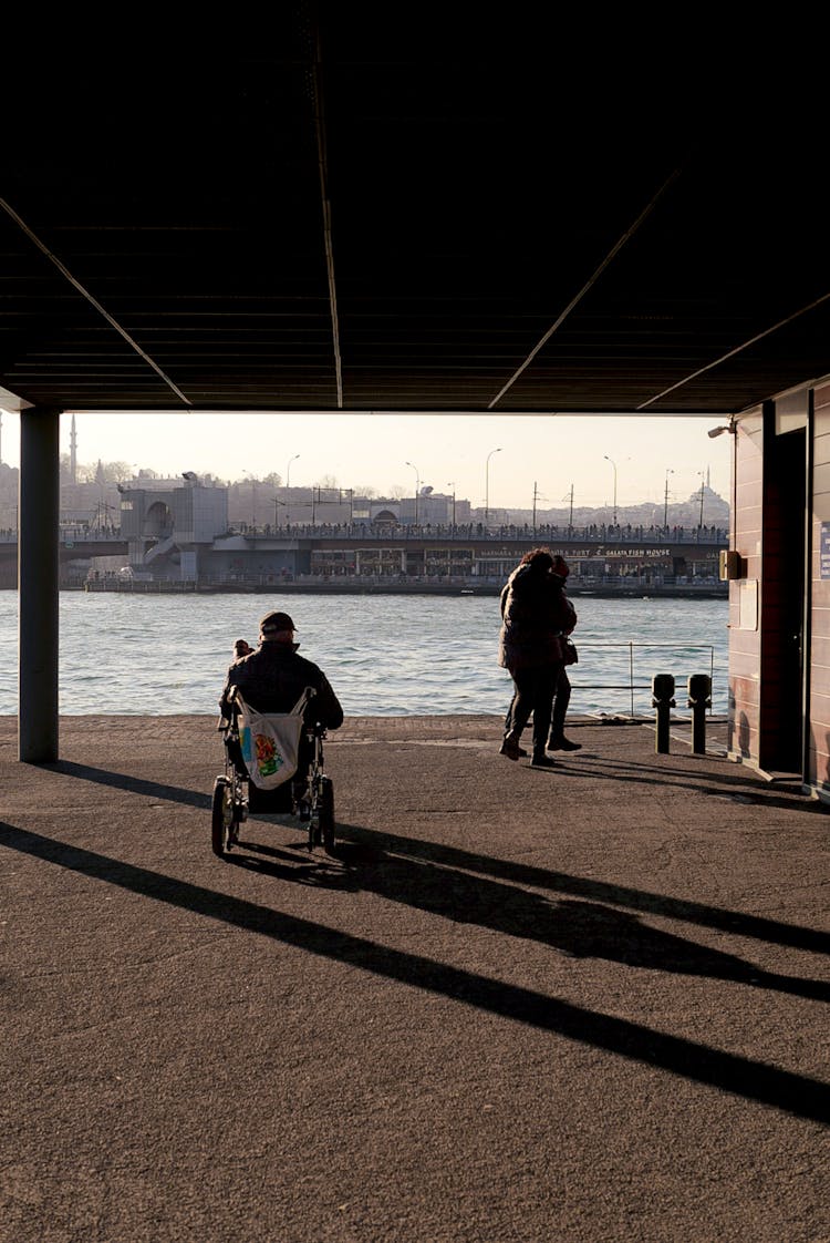 People And Man On Wheelchair On Shore In Istanbul With Galata Bridge Behind