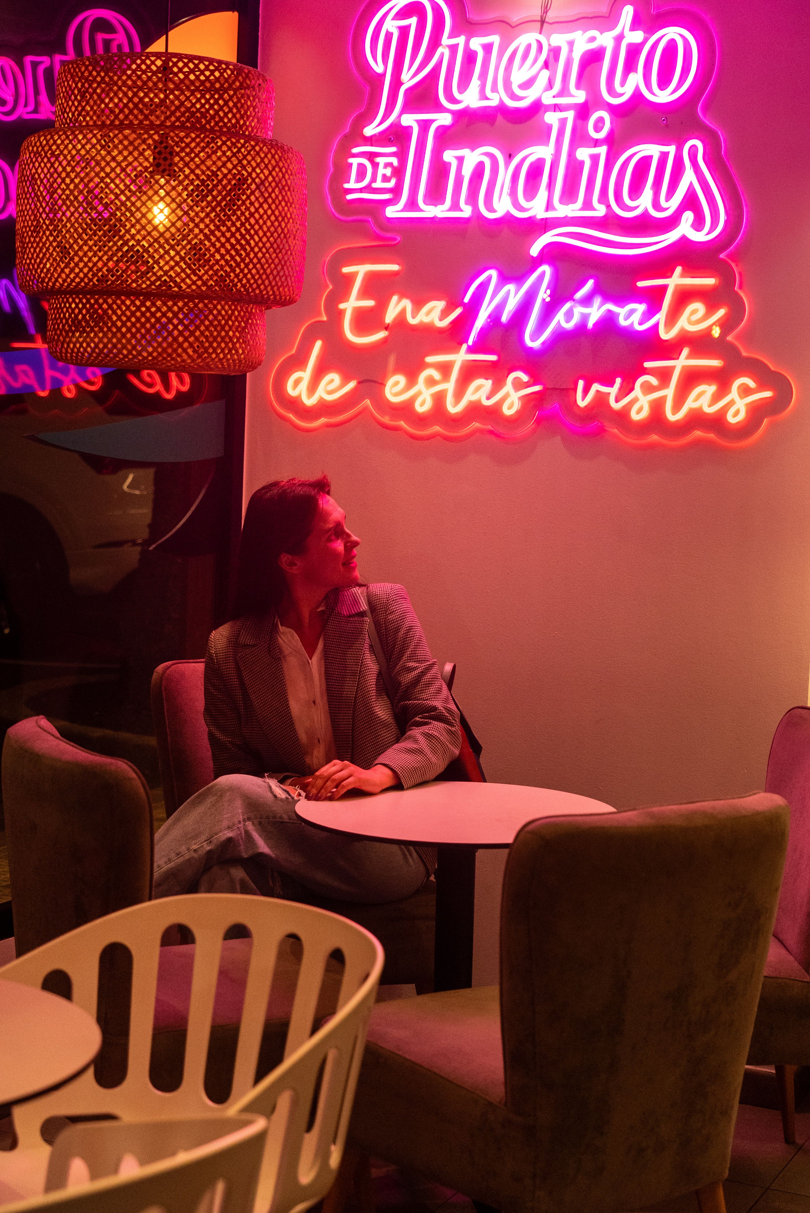 Woman in suit jacket sits in a modern cafe with vibrant neon signs.