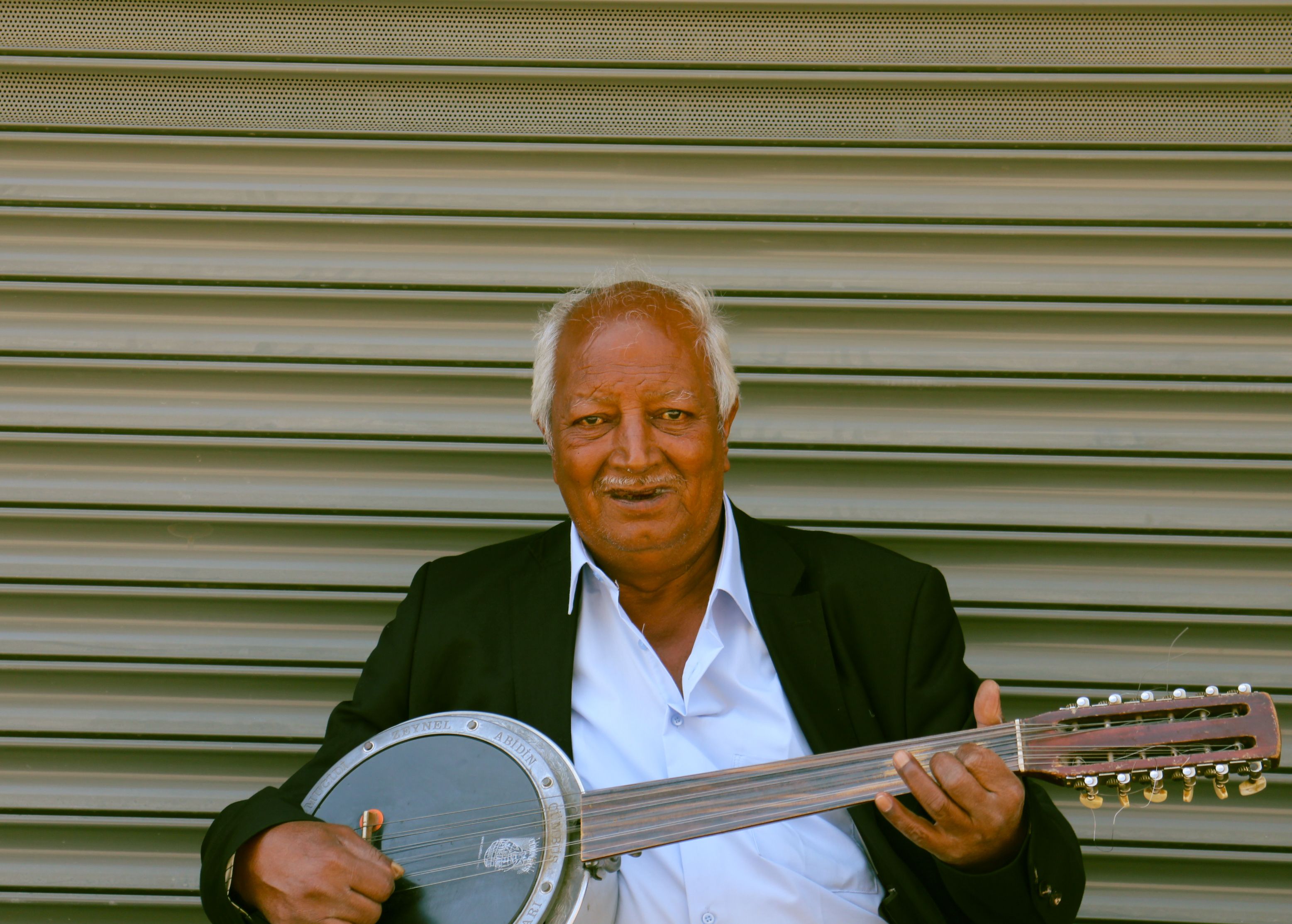 Elderly man in suit playing traditional string instrument outdoors.