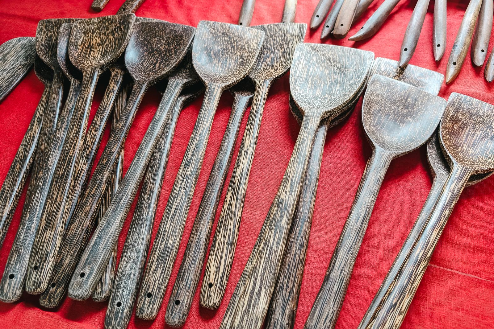 A collection of handcrafted wooden kitchen utensils displayed on a vibrant red background.