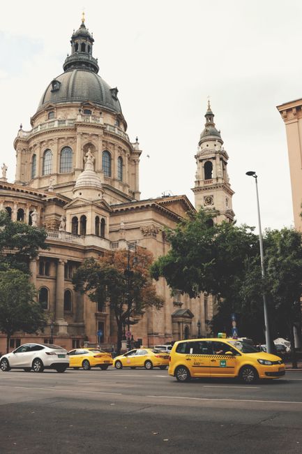 View of St. Stephen's Basilica in Budapest with yellow taxis passing by, emphasizing urban life.