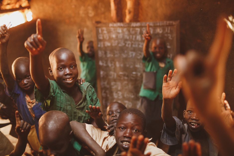 Children raising hands in classroom in Uganda