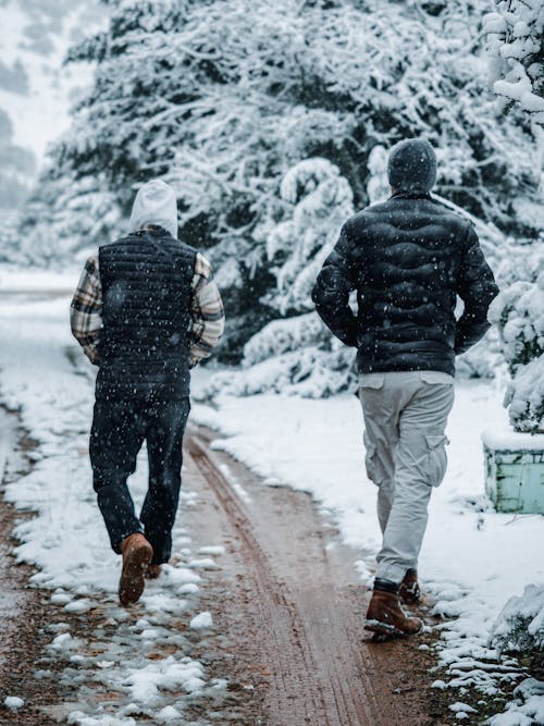 Back View of Man Walking on Dirt Road in Snow