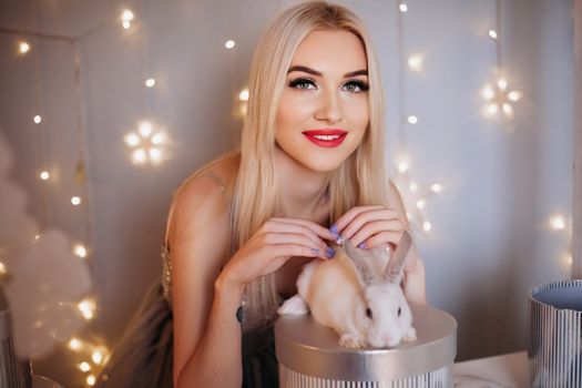 Blonde woman smiling with a white rabbit and festive fairy lights in Sofia, Bulgaria.