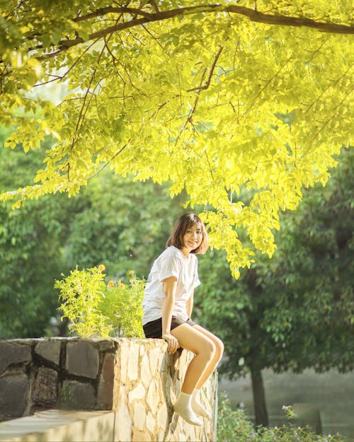 Young Woman Sitting on a Wall in a Park 