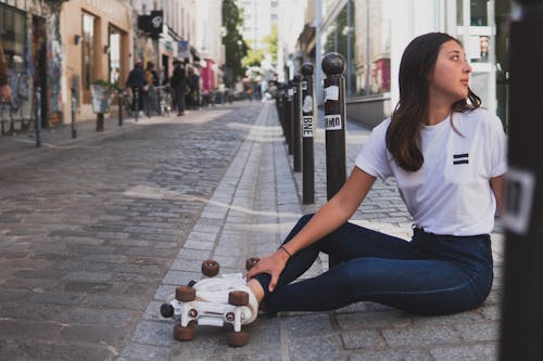 Free A Woman in White Shirt and Denim Jeans Sitting on Sidewalk Stock Photo
