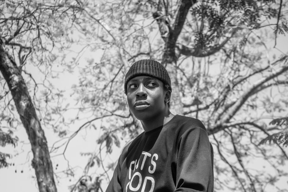 A black and white portrait of a man wearing a beanie outdoors with trees in the background.