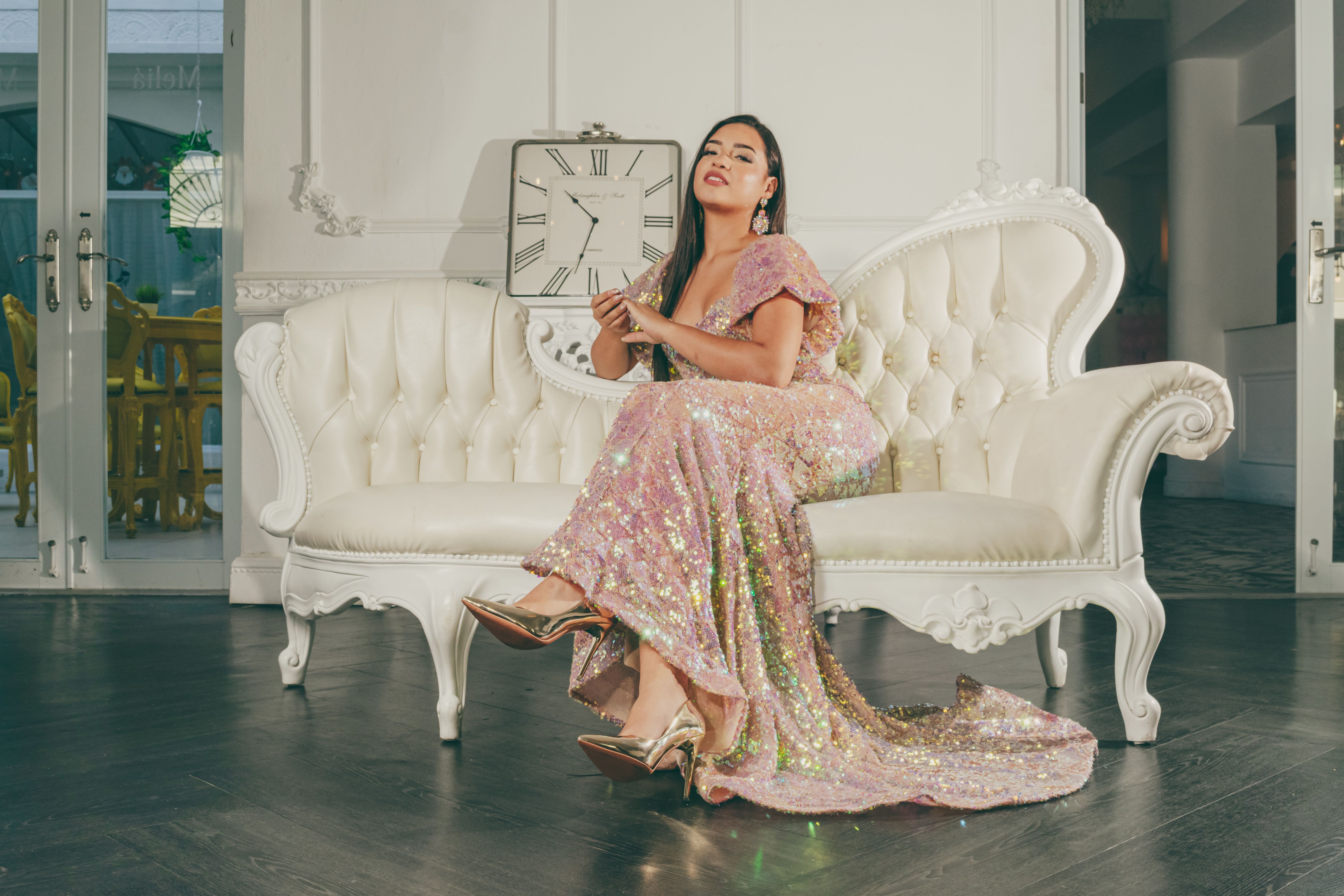 Portrait of a woman in a sparkling dress sitting on an elegant white sofa indoors.