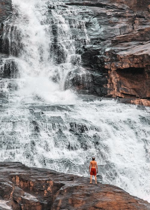 A Shirtless Man Standing Near Cascading Waterfall