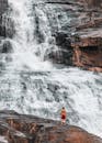 一个赤膊的男人勇敢地站在岩石上，凝视着雄伟的瀑布