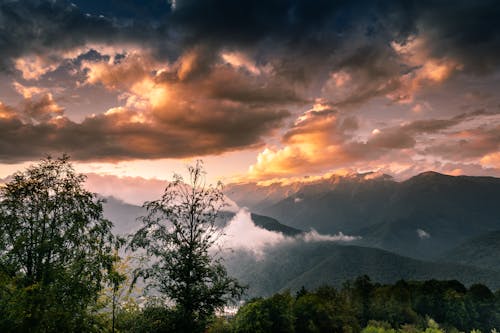 A sunset over the mountains with clouds and trees