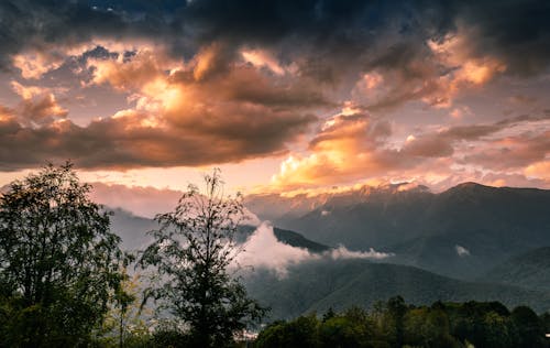 A sunset over the mountains with clouds and trees