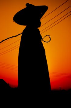Dramatic silhouette of a man in sombrero against a vibrant sunset sky, evoking mystery and culture.