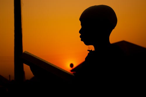 Silhouette of a Boy Reading a Book at Sunset 