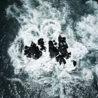 Aerial view of surf breaking over dark rocks. Photo by Joem Castillo on Pexels.