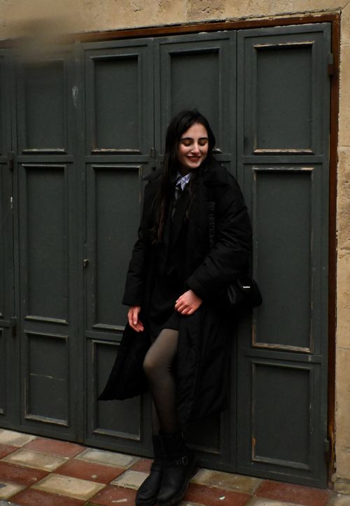 Free Stylish woman in black jacket posing against a rustic door in urban setting. Stock Photo