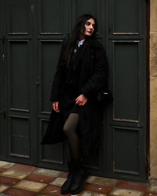 Young Brunette in a Black Coat Standing against a Wall 