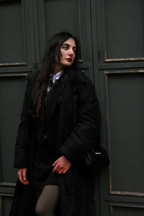 Free A fashionable woman in a black coat poses against a dark wall, showcasing modern elegance. Stock Photo