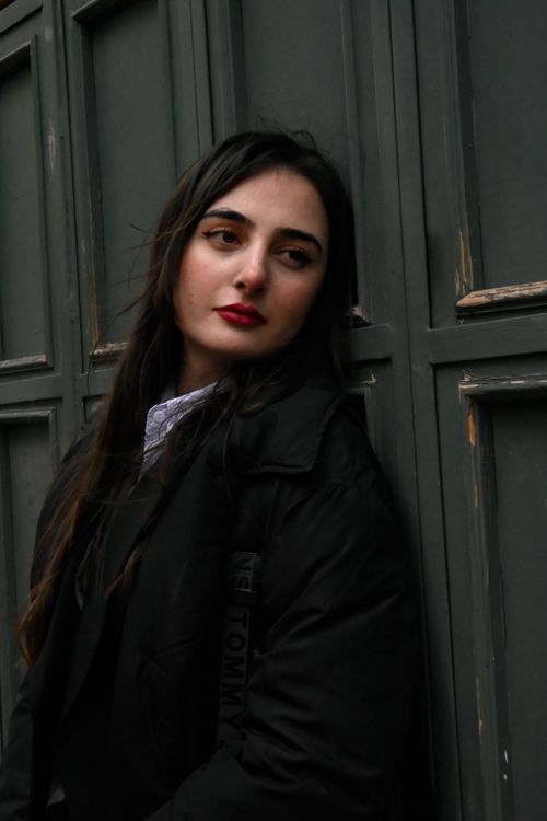 Free Portrait of a young woman with red lips in a black jacket, leaning against a textured wall. Stock Photo