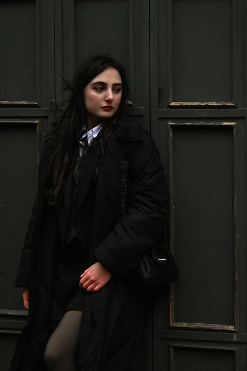 Young Brunette in a Black Coat Standing against a Wall 