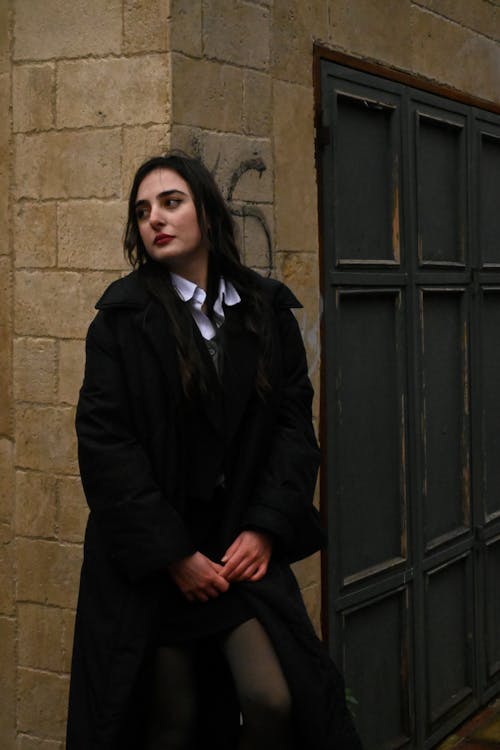 Young Woman in a Black Coat Standing near a Building in City 