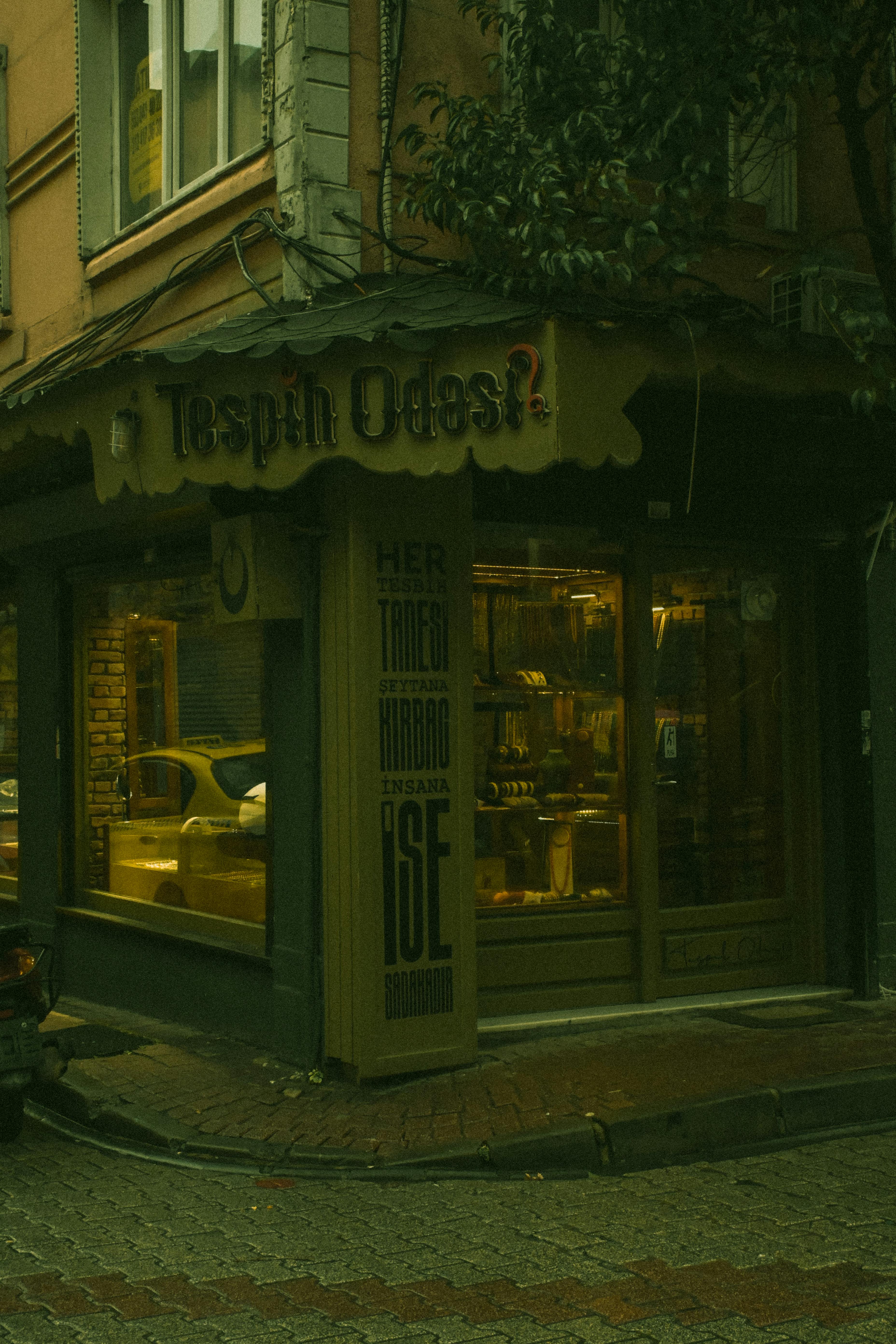Free A charming corner shop with a warmly lit interior located on a city street at night. Stock Photo