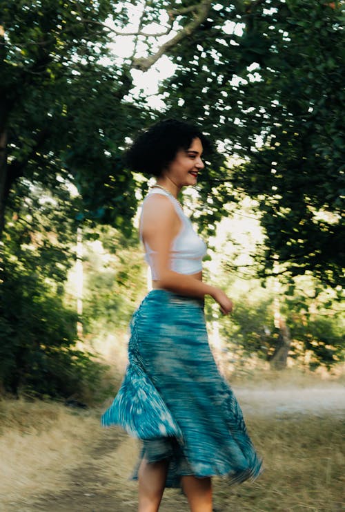 Young Woman in a Tank Top and Skirt Standing on a Meadow and Smiling 