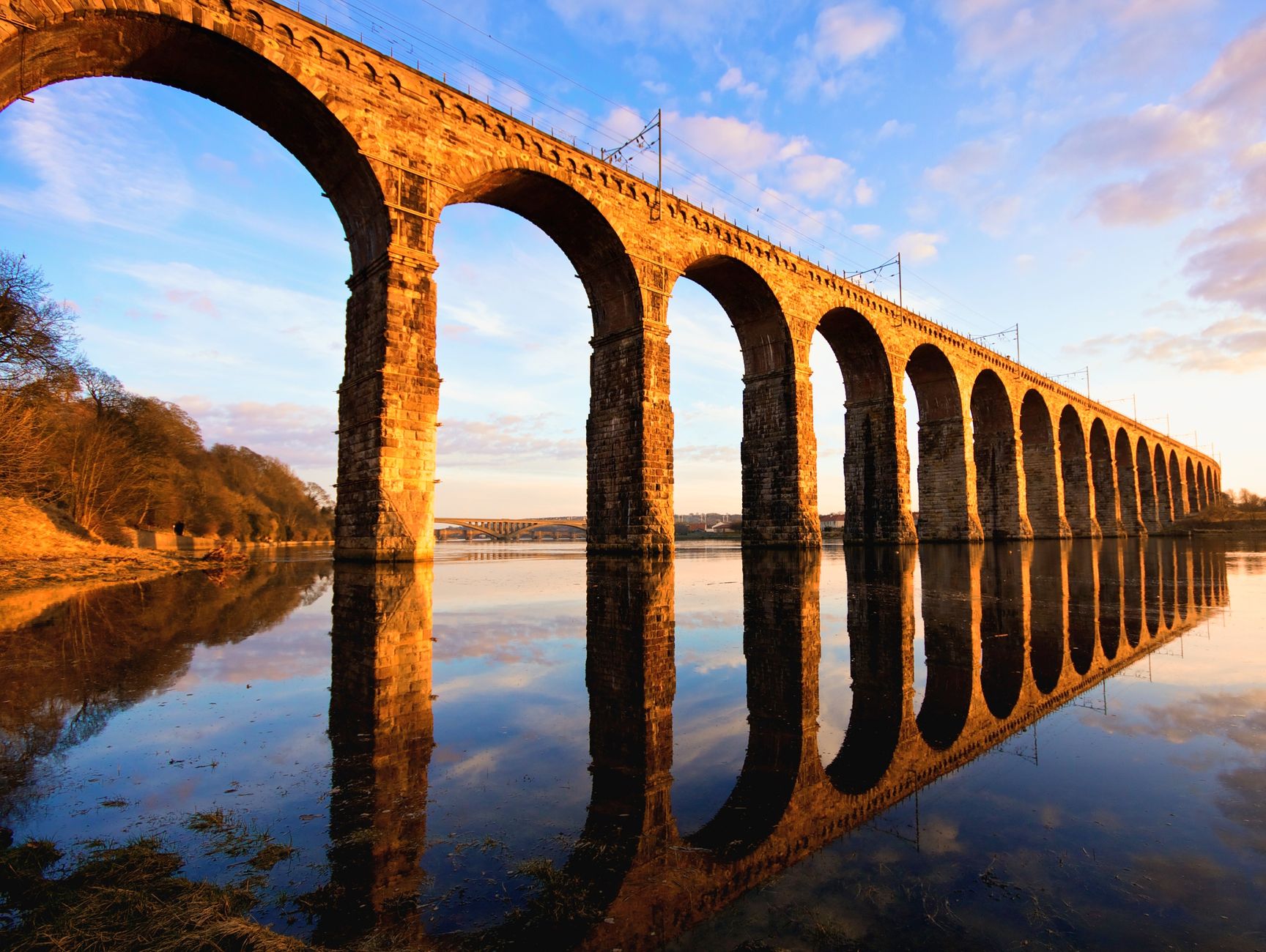 Berwick-upon-Tweed's Royal Border Bridge reflecting in the River Tweed at sunset, Northumberland, England