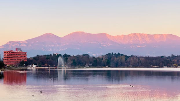 Peaceful sunset over Tirana lakefront with mountains in the backdrop and a fountain creating a picturesque scene.