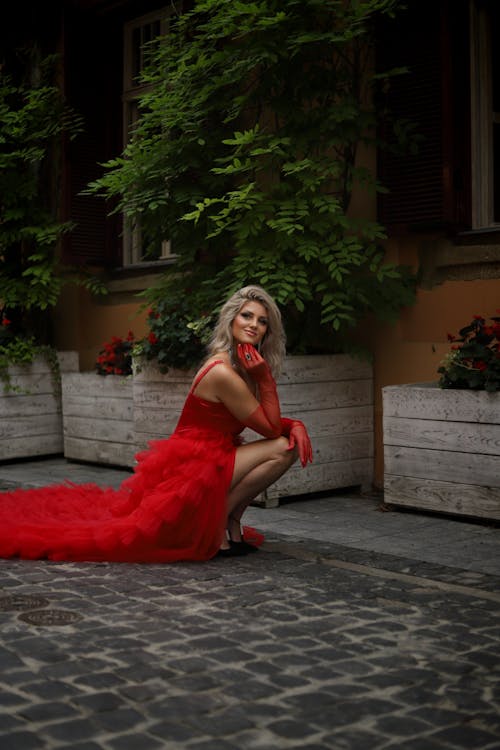 Woman in Red Dress Squatting on Cobblestone Street