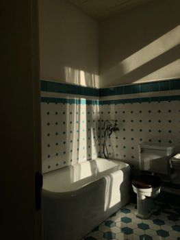 Sunlit bathroom with a white bathtub, teal tiles, and soft shadows.