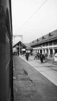 Black and white photo of a busy urban train station with people and buildings.