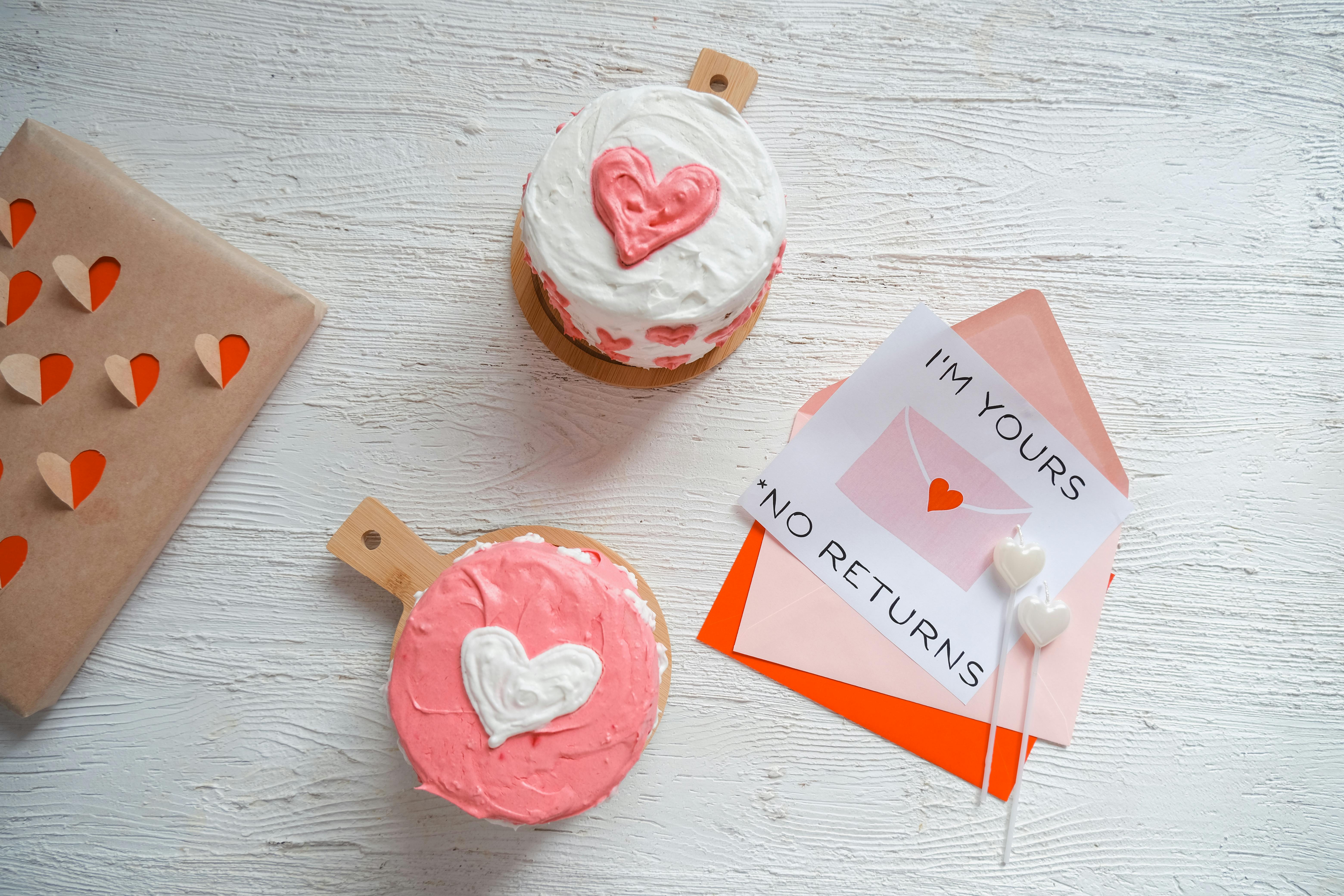 Top view of heart-shaped cakes and romantic notes on a white wooden background, perfect for Valentine's Day.