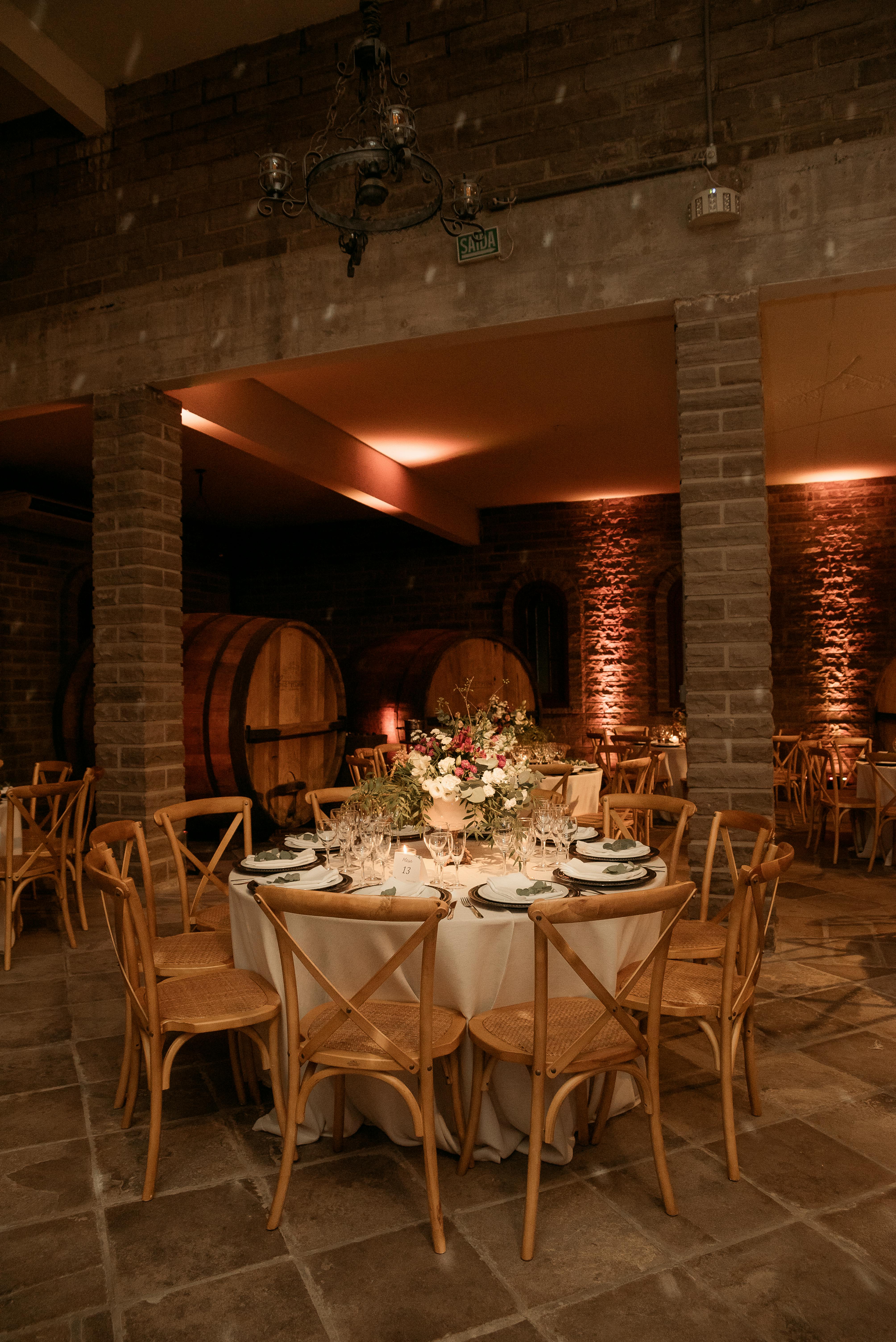 Free Beautifully decorated table setting in a cozy wine cellar with wooden chairs and ambient lighting. Stock Photo