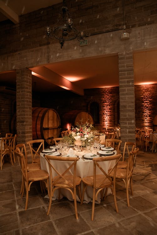 Free Beautifully decorated table setting in a cozy wine cellar with wooden chairs and ambient lighting. Stock Photo