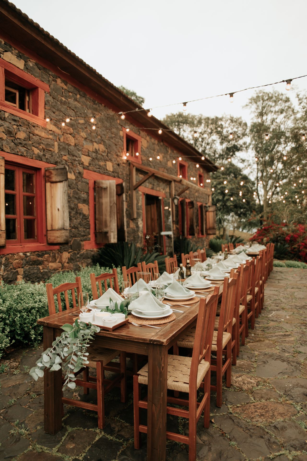 Une table rustique en extérieur près d'une maison en pierre, sous une guirlande lumineuse.