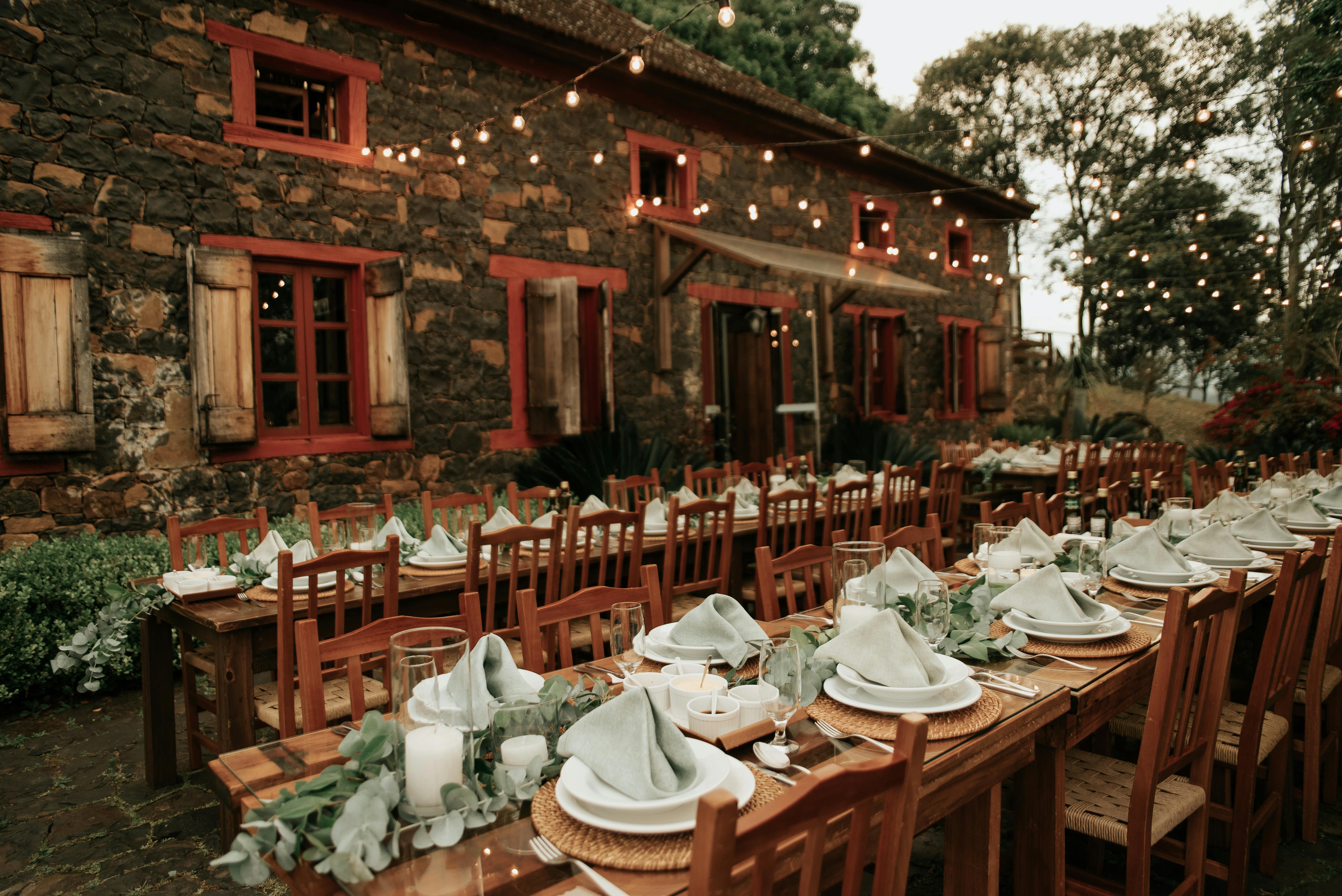 Outdoor rustic dinner setting with string lights, wooden tables, and stone building, creating a warm ambiance.