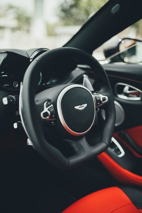 Free Close-up of a luxury sports car steering wheel with red interior accents, showcasing elegance and sophistication. Stock Photo