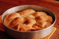 Golden brown bread rolls perfectly baked in a round metal pan, sitting on a wooden table.