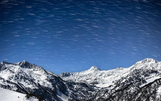 Stunning Pyrenees mountain range under a vibrant night sky with star trails in winter.