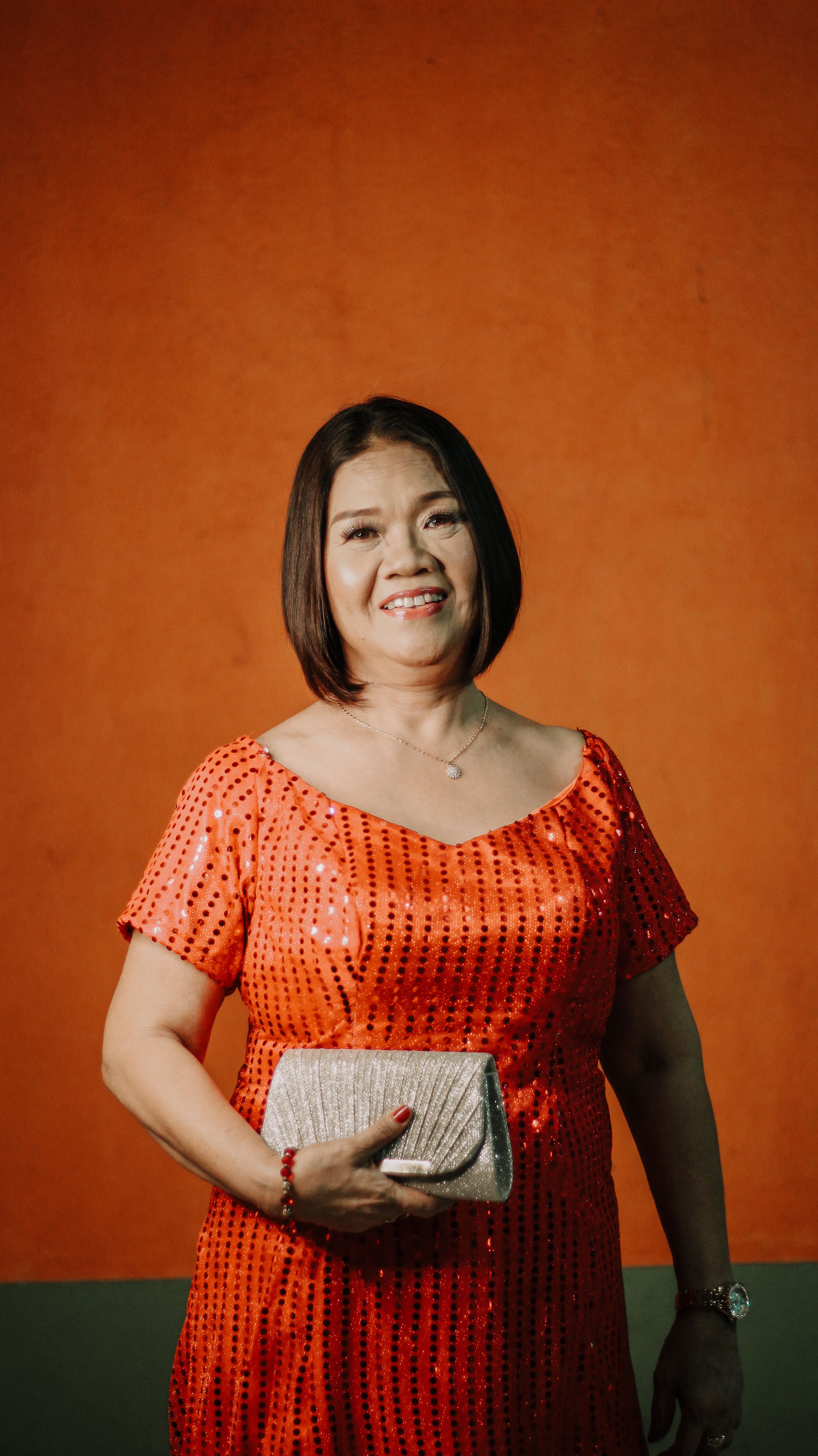Smiling woman in an elegant orange dress with a clutch against an orange background.