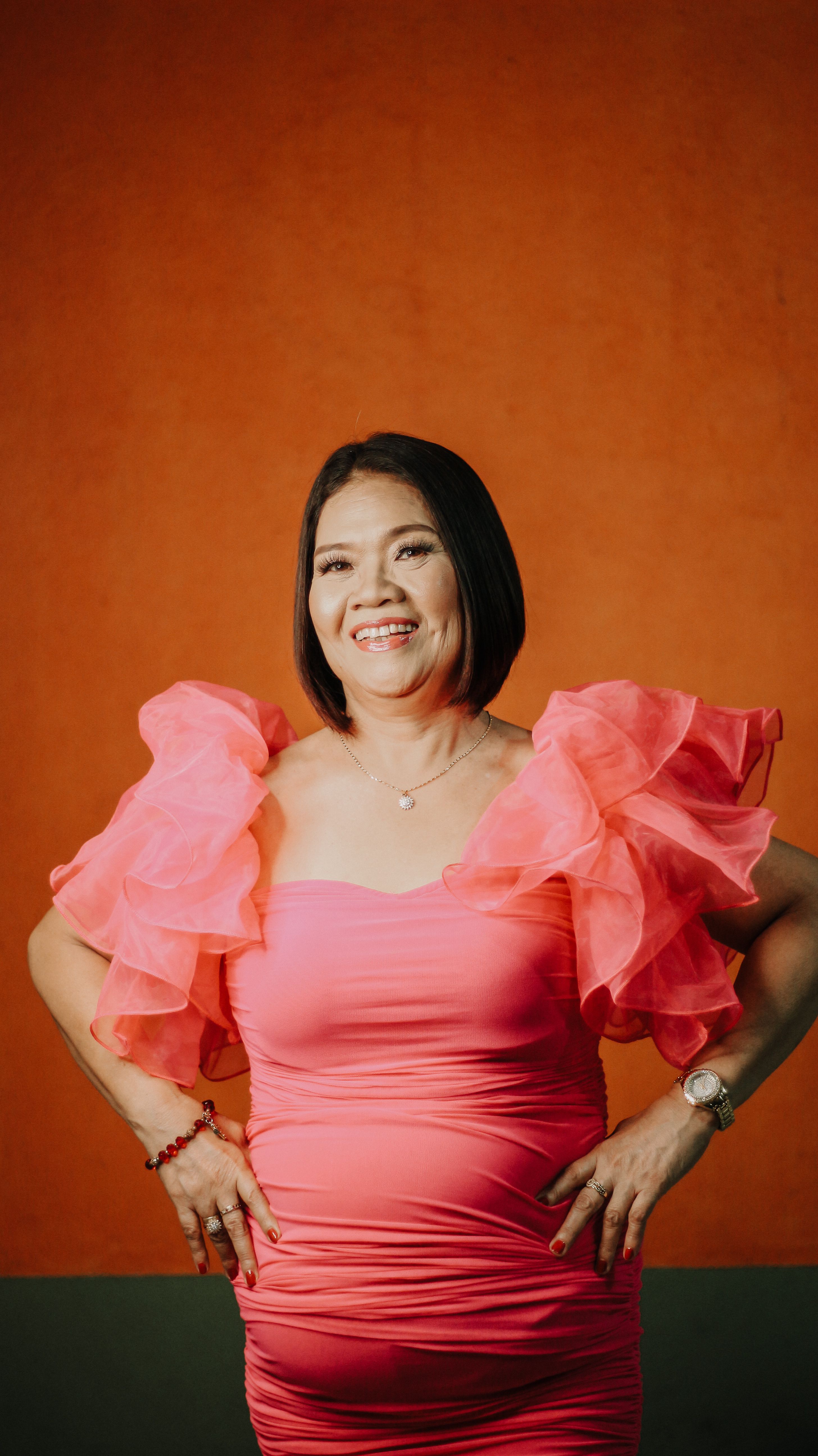 Portrait of an Asian woman in a vibrant pink dress against an orange background, exuding confidence and elegance.