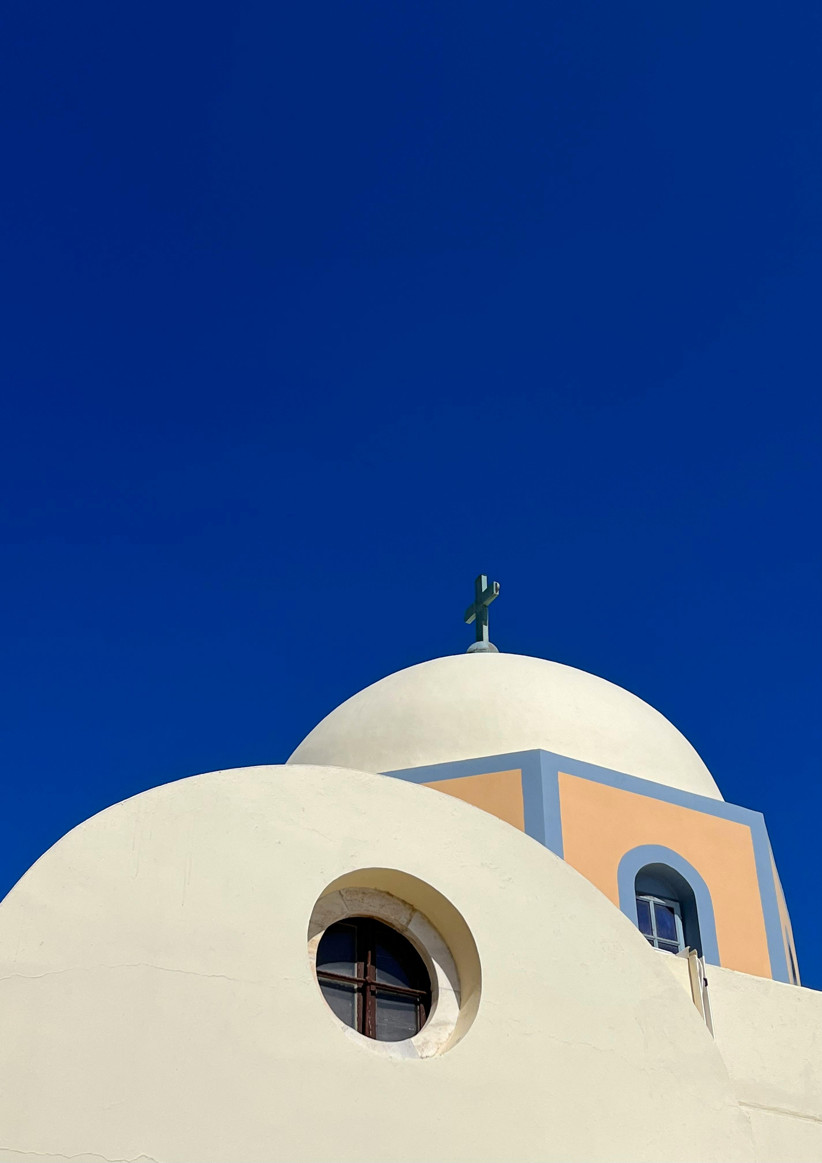 A striking white dome church with a cross under a bright blue sky, symbolizing peace.