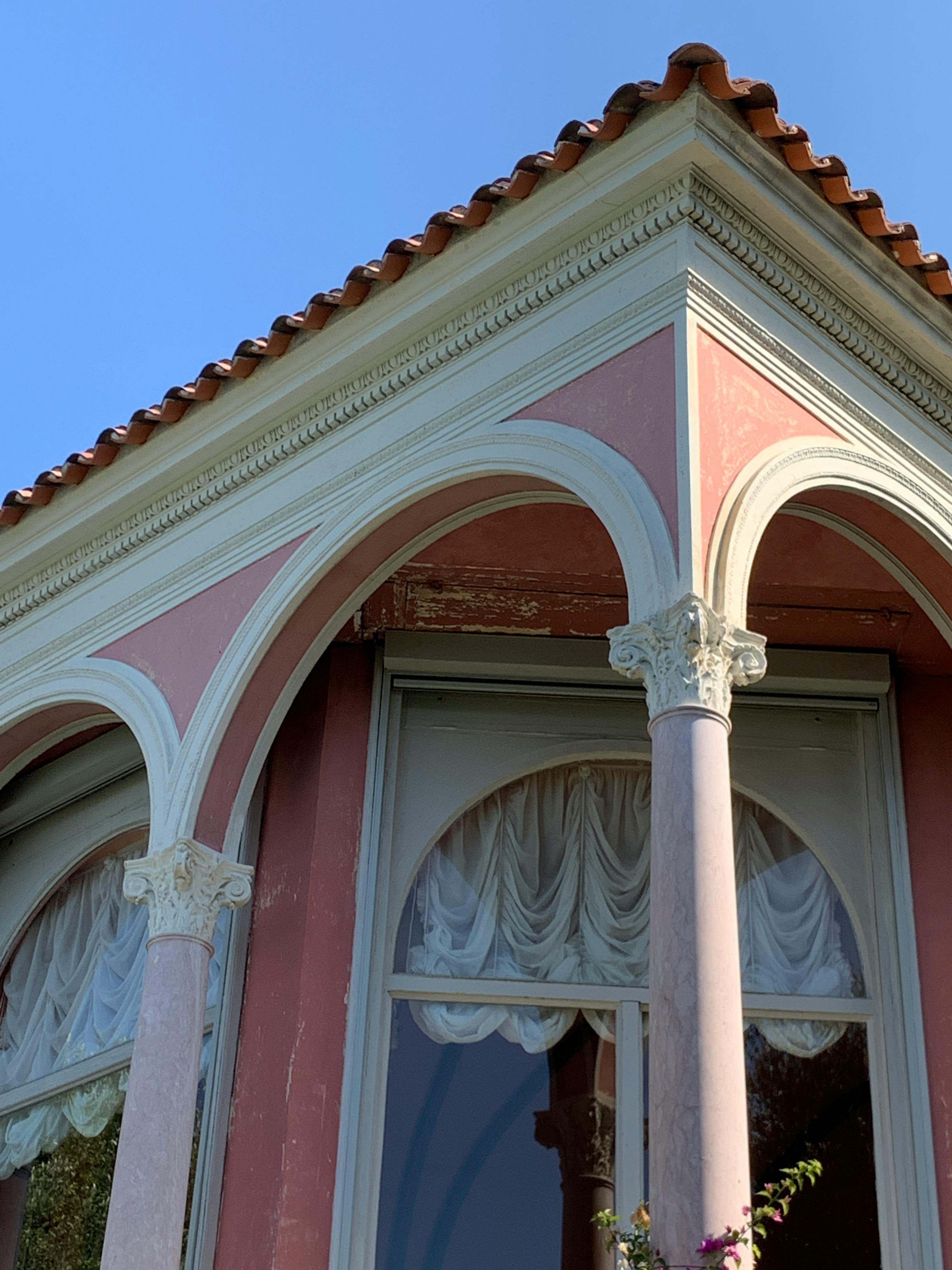 Elegant pink building facade with arches and windows, sunlit on a summer day.